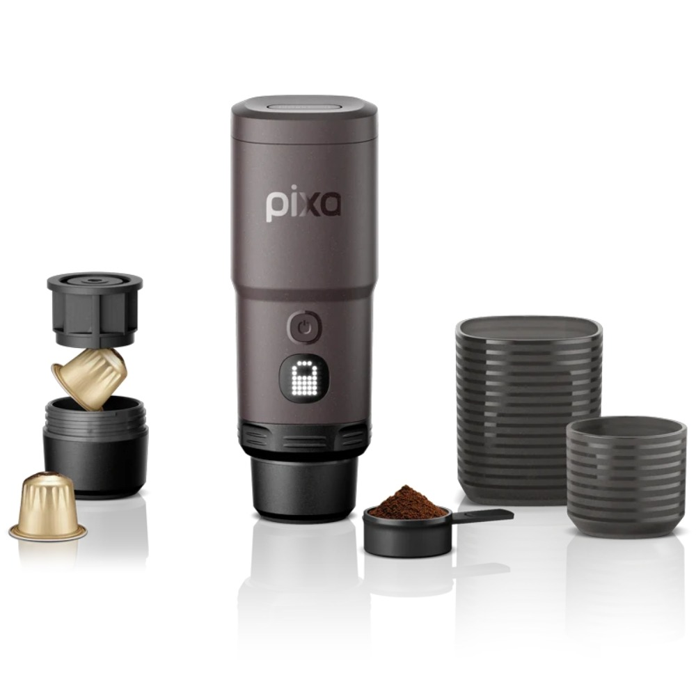 Eine tragbare Pixa-Kaffeemaschine mit Goldkapseln, Kaffeemehl im Löffel und zwei Tassen auf weißem Hintergrund.