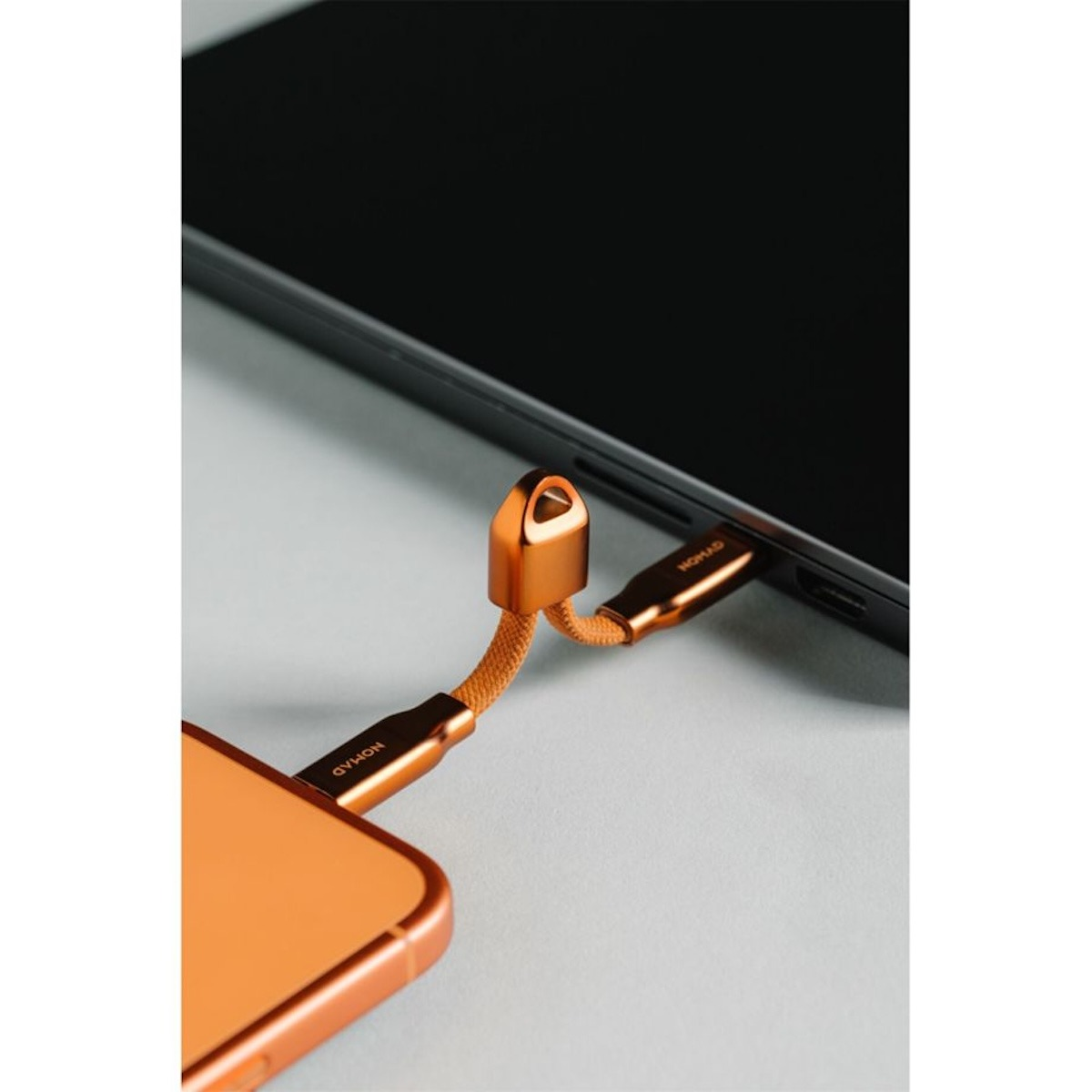 Ein orangefarbenes Ladekabel verbindet ein Smartphone mit einem Laptop auf einer grauen Oberfläche.