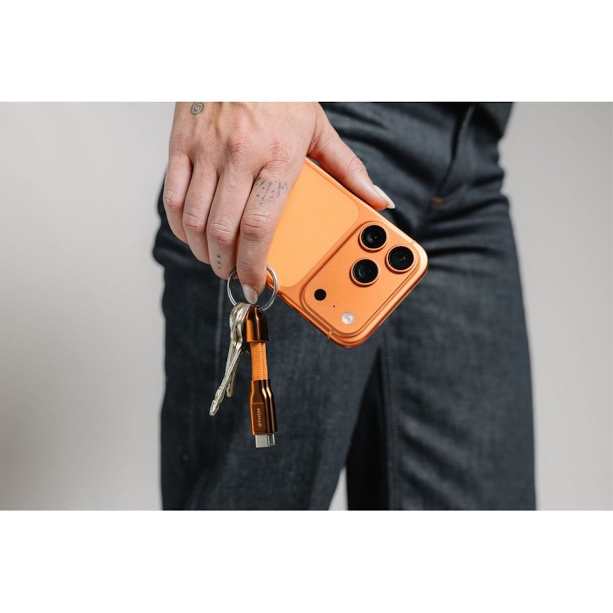 Eine Person hält ein orangefarbenes Handy und einen Schlüsselring mit Schlüsseln und Ladekabel.