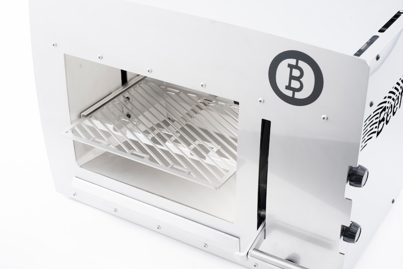 Ein weißes Elektrogerät mit offenem Fach und einem metallenen Grillgitter im Inneren, auf hellem Hintergrund.