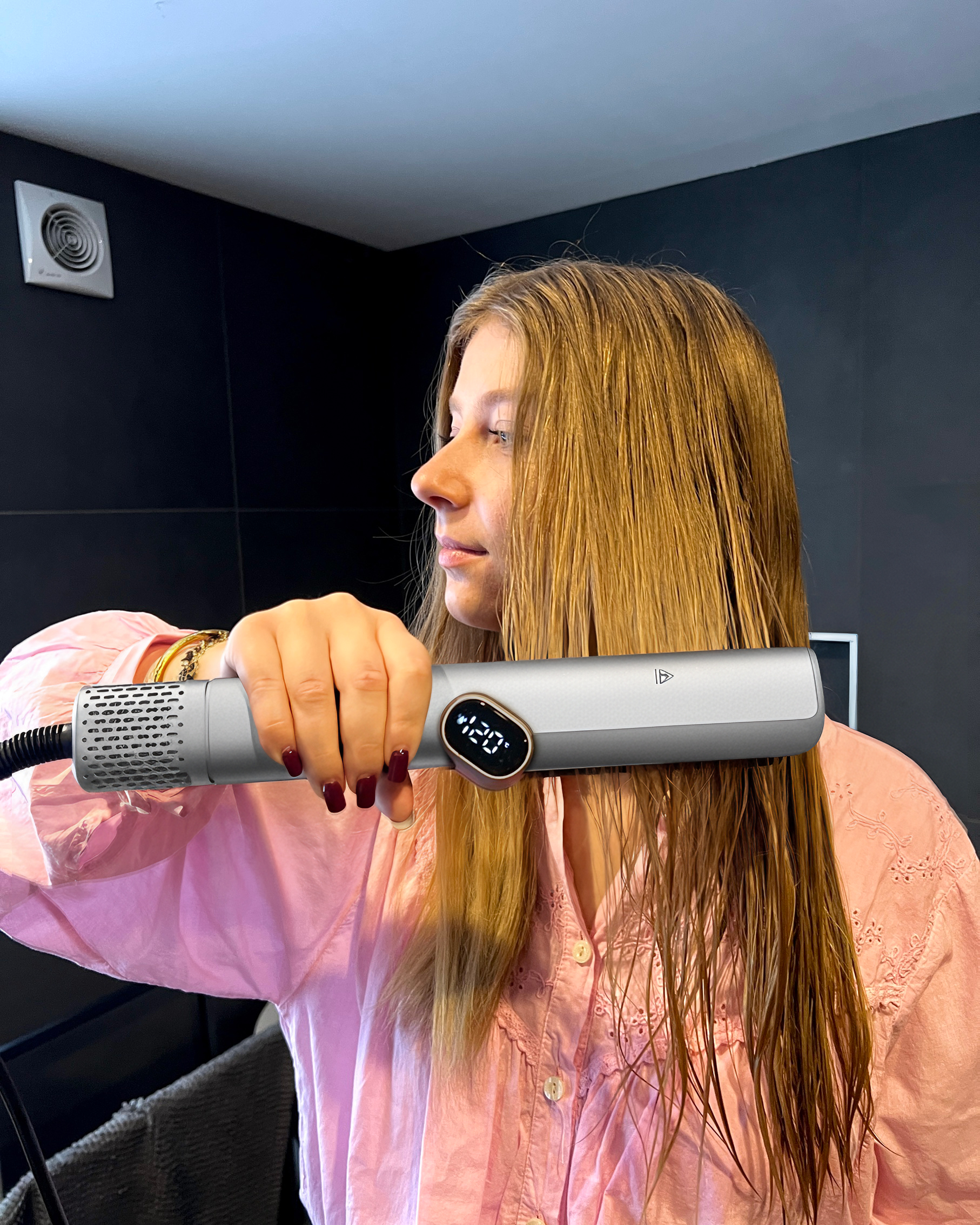 Una donna in rosa asciuga i suoi lunghi capelli biondi con un piastra grigia.