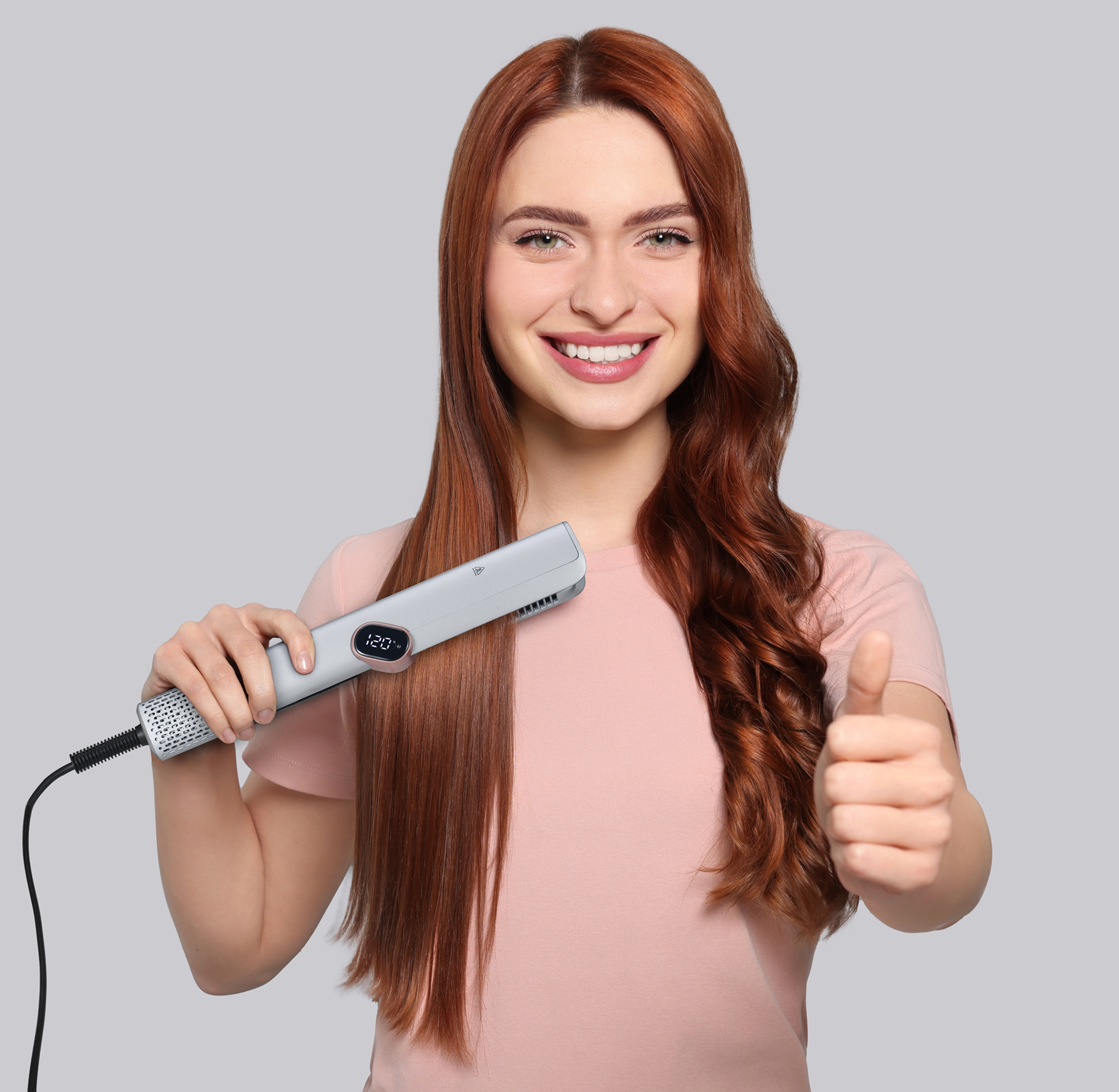 Donna dai capelli rossi sorridente con piastra per capelli, mostra capelli lisci e ricci, pollice in alto.