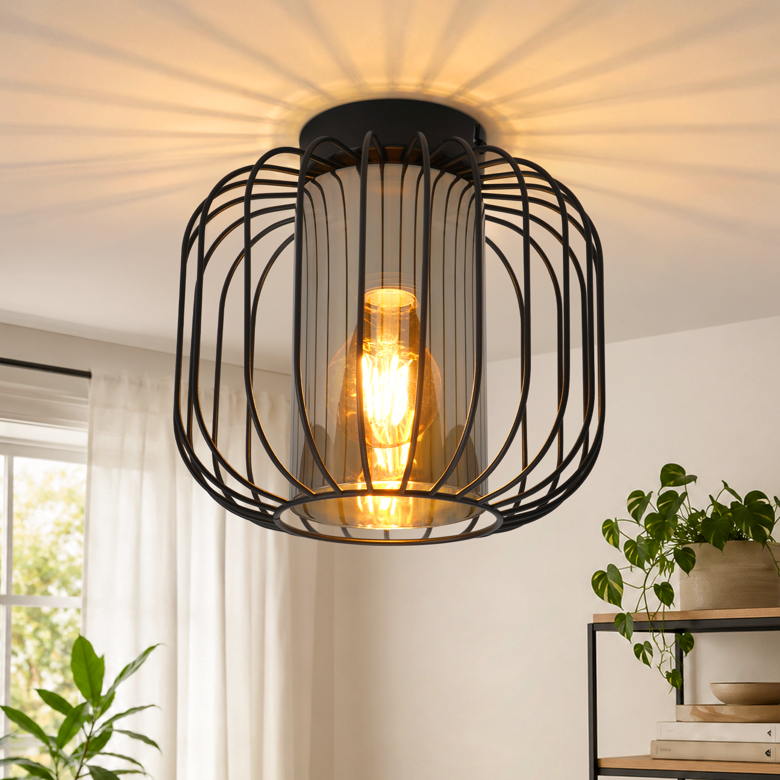 Czarna metalowa lampa sufitowa z żarówką rzuca wzory cieni na biały sufit.