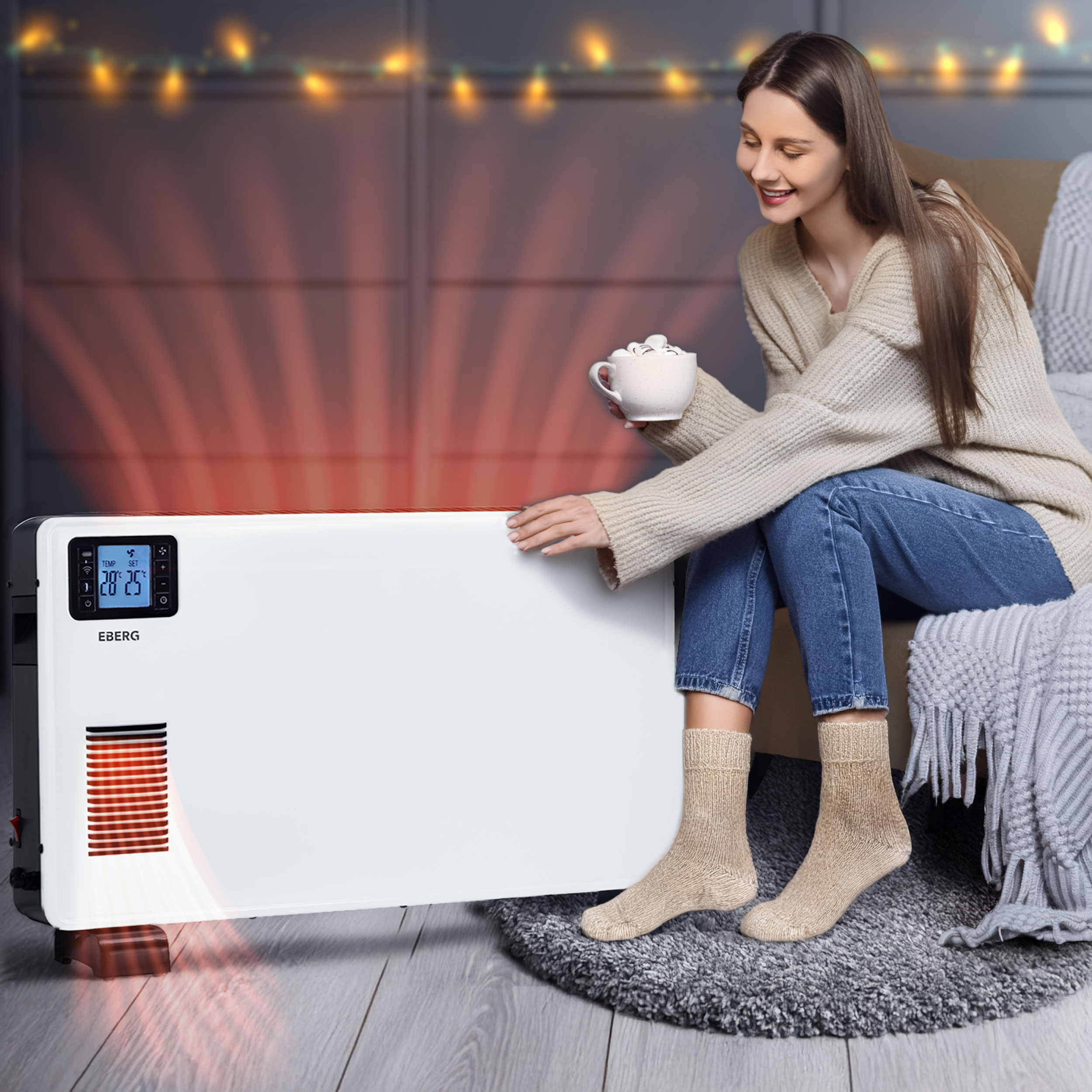 Kobieta z kubkiem siedzi w cieple przy białym grzejniku elektrycznym z czerwonymi falami ciepła.