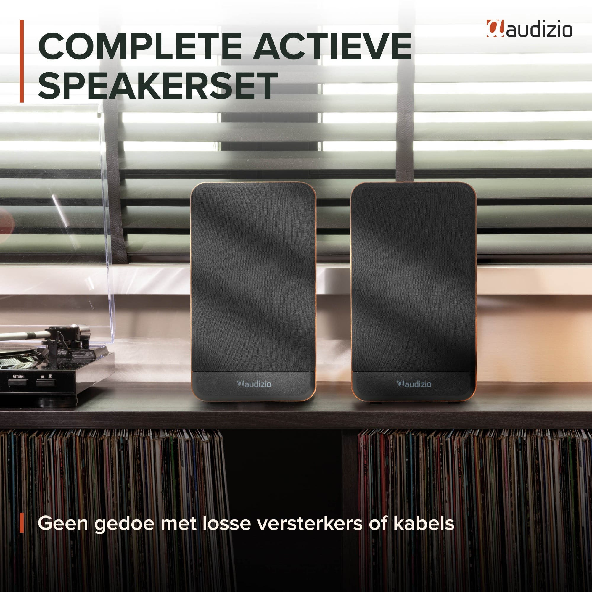 Dos altavoces activos Audizio negros sobre una consola de madera frente a estantes de discos y persianas.
