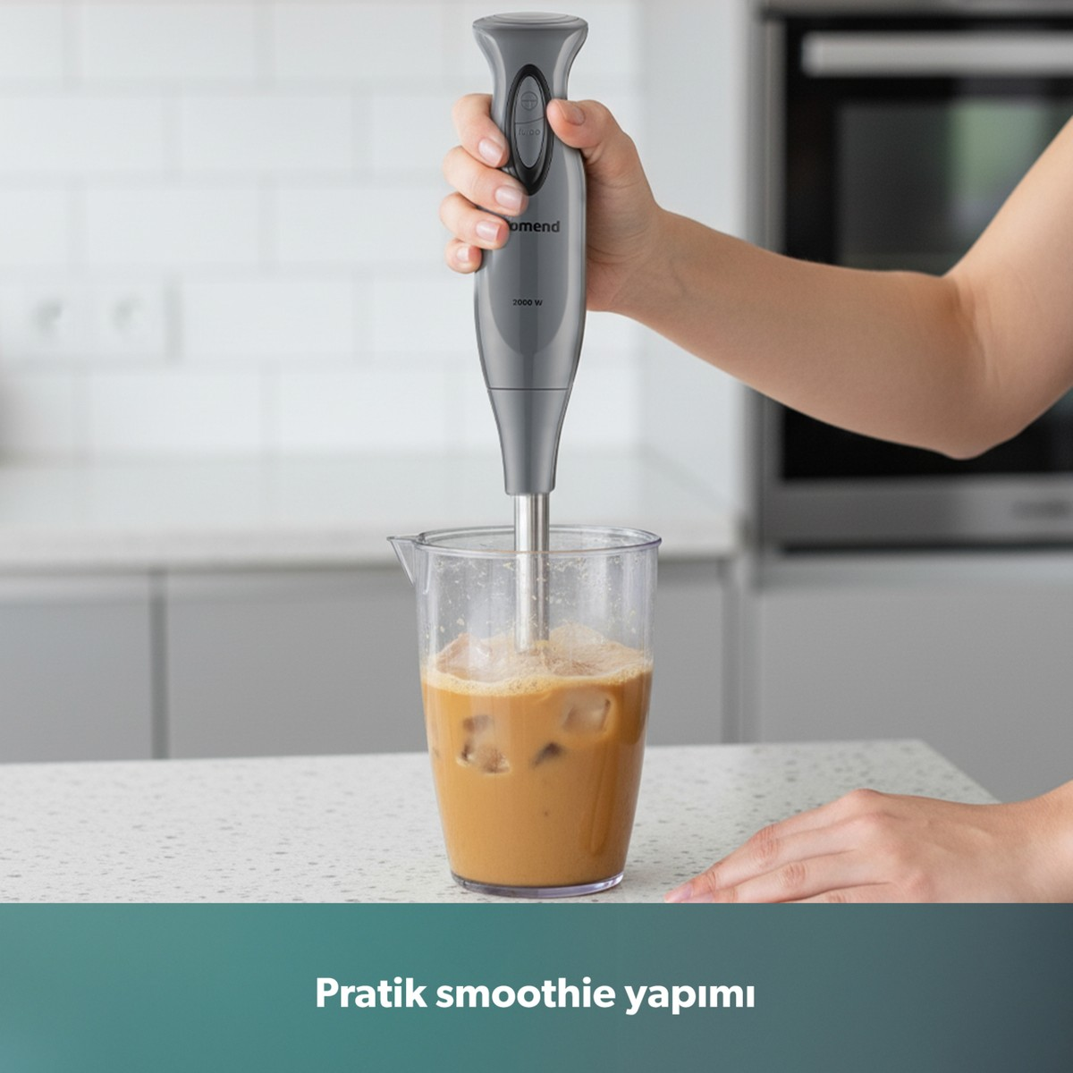 Bir el, beyaz mutfak arka planında, bir bardaktaki buzlu kahveyi karıştıran gri bir blender tutuyor.