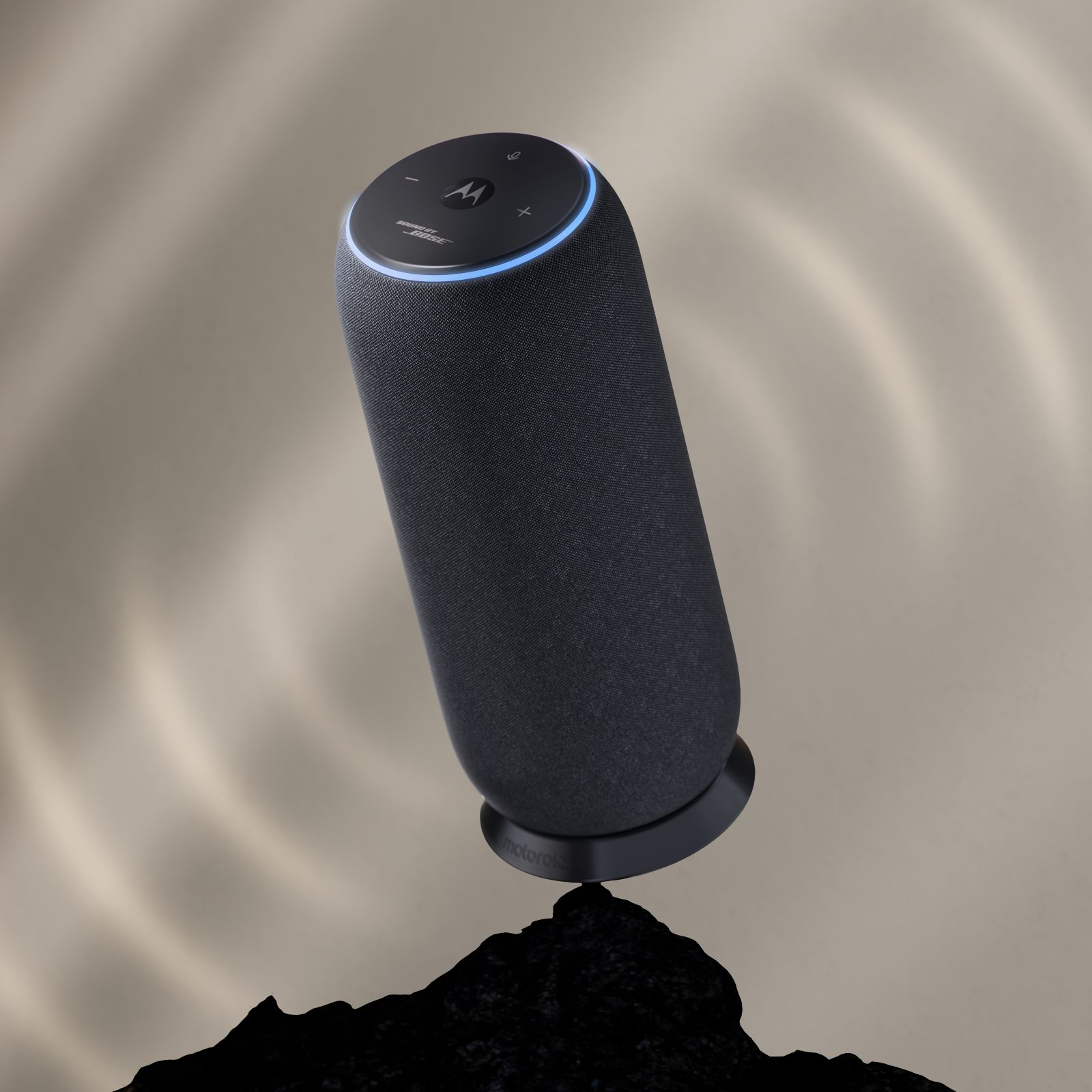 Un altoparlante intelligente nero con un anello blu luminoso poggia su una roccia scura con sfondo beige.