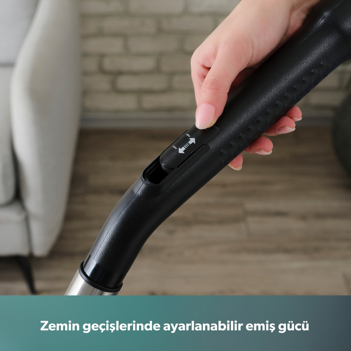 Bir el, siyah elektrik süpürgesi sapındaki emiş gücü sürgüsünü ayarlıyor, arka planda bulanık bir oda var.
