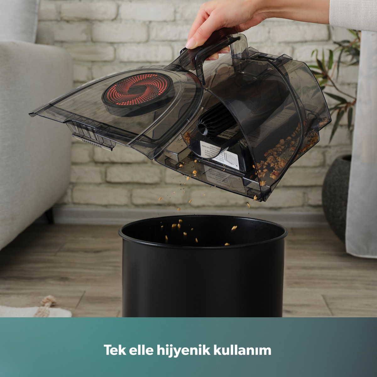 Bir el, elektrikli süpürgenin toz haznesini siyah çöp kovasına boşaltıyor.