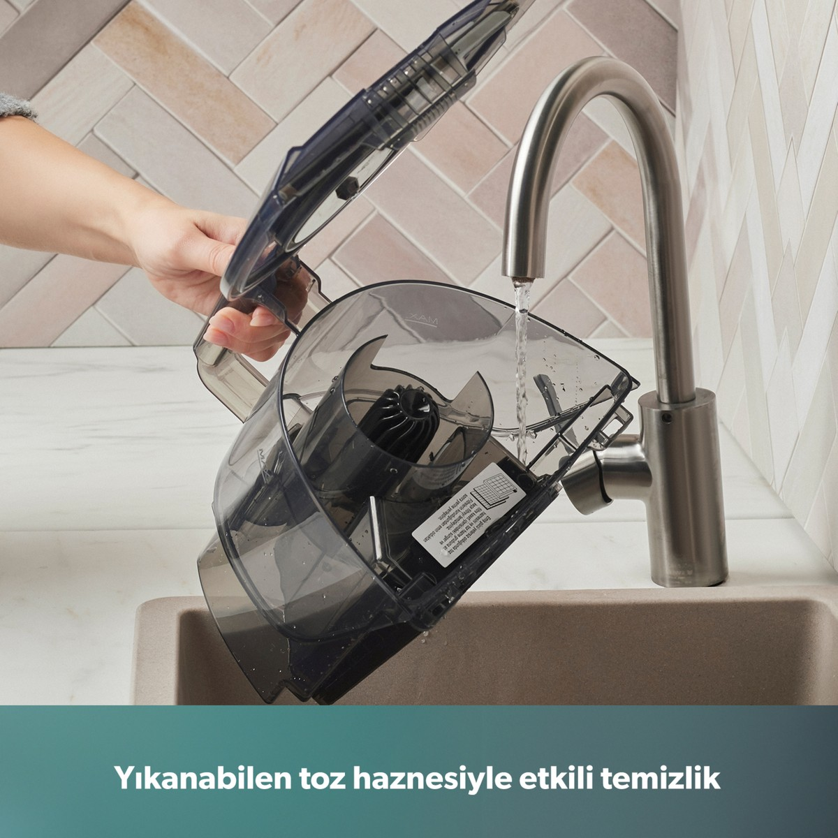 Bir kişi mutfak musluğundan akan su altında süpürgenin toz haznesini duruluyor.