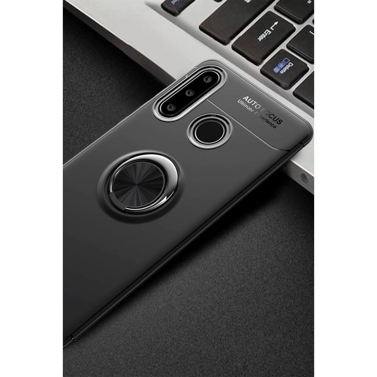 Arkasında halka tutucu olan siyah akıllı telefon kılıfı, koyu renkli bir yüzeyde laptop klavyesinin yanında duruyor.