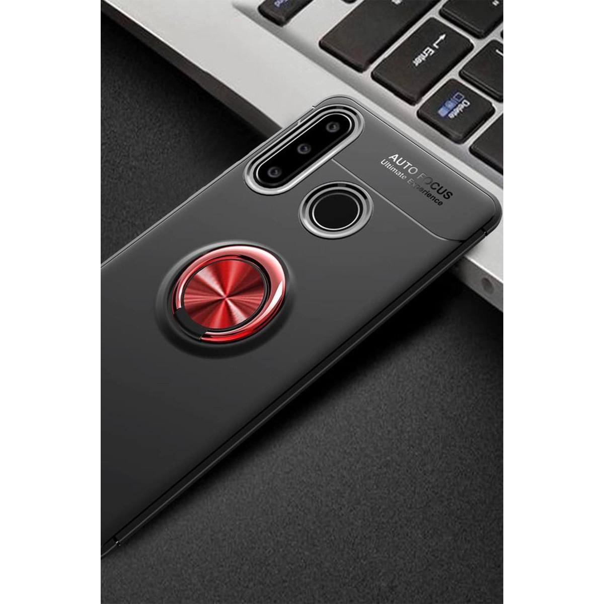 Gri bir yüzeyde, klavye yakınında kırmızı halka tutuculu siyah akıllı telefon kılıfı.