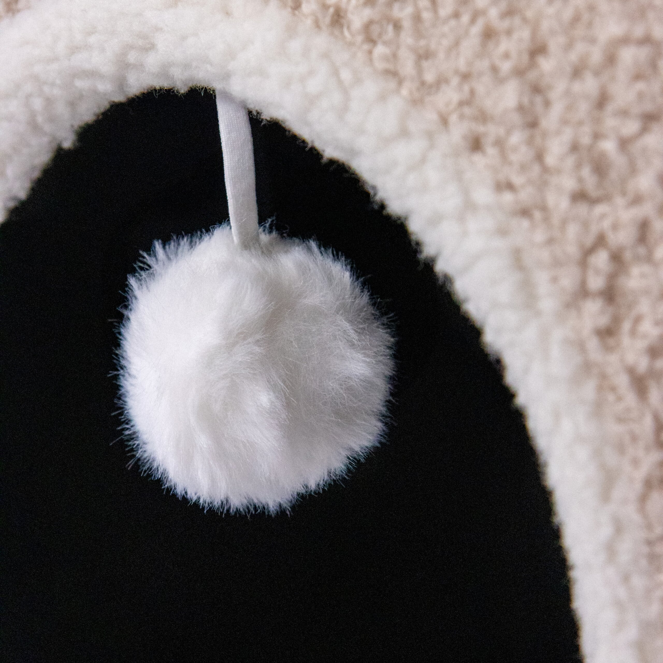 Ein flauschiger weißer Pompon hängt an einem weißen Band von einem hellen, plüschigen Bogen vor schwarzem Hintergrund.