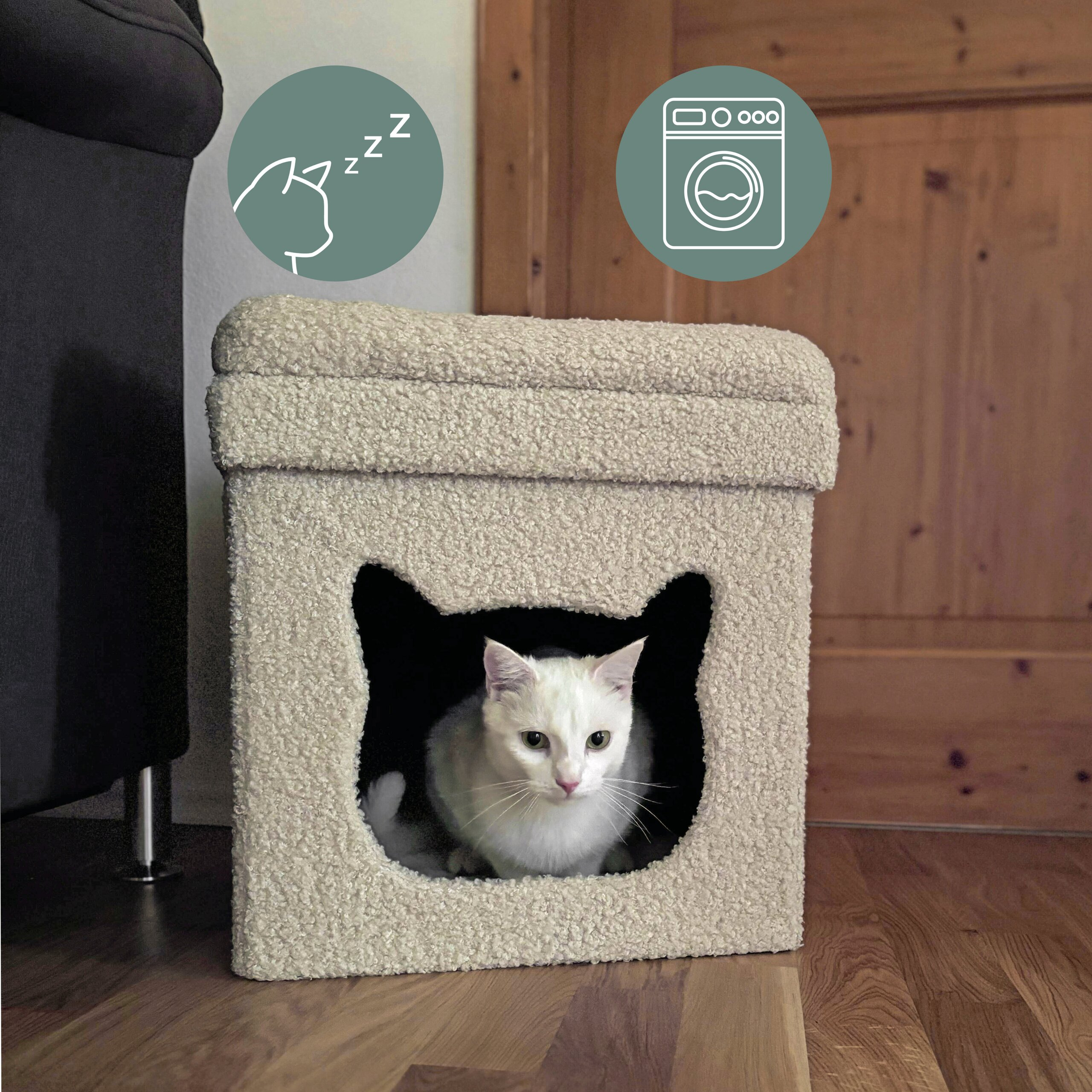 Eine weiße Katze sitzt in einem beigen, flauschigen Katzenhaus mit katzenförmigem Eingang.