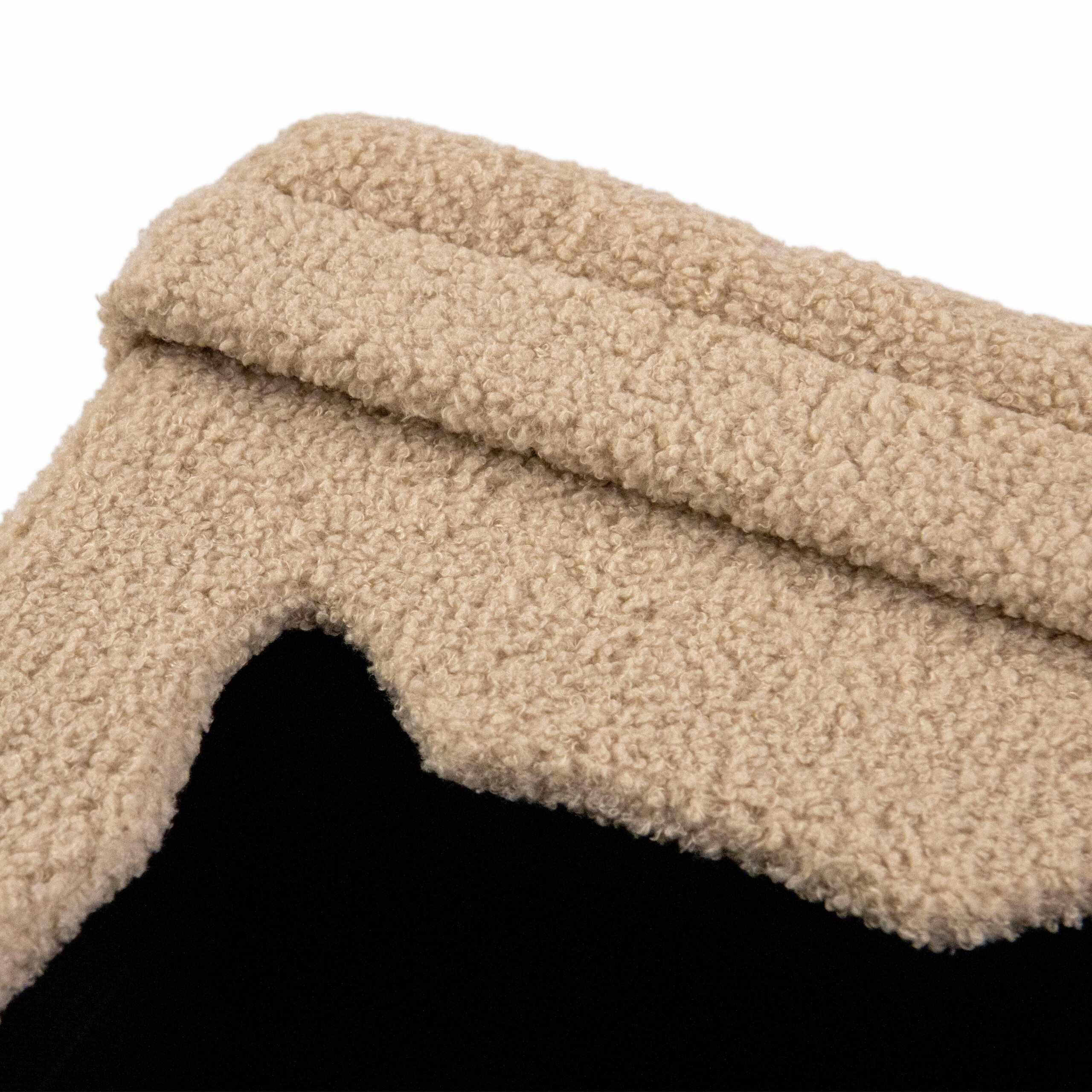 Nahaufnahme eines beigen Futterstoffes aus Teddy-Fleece mit einer schwarzen Textilschicht darunter.