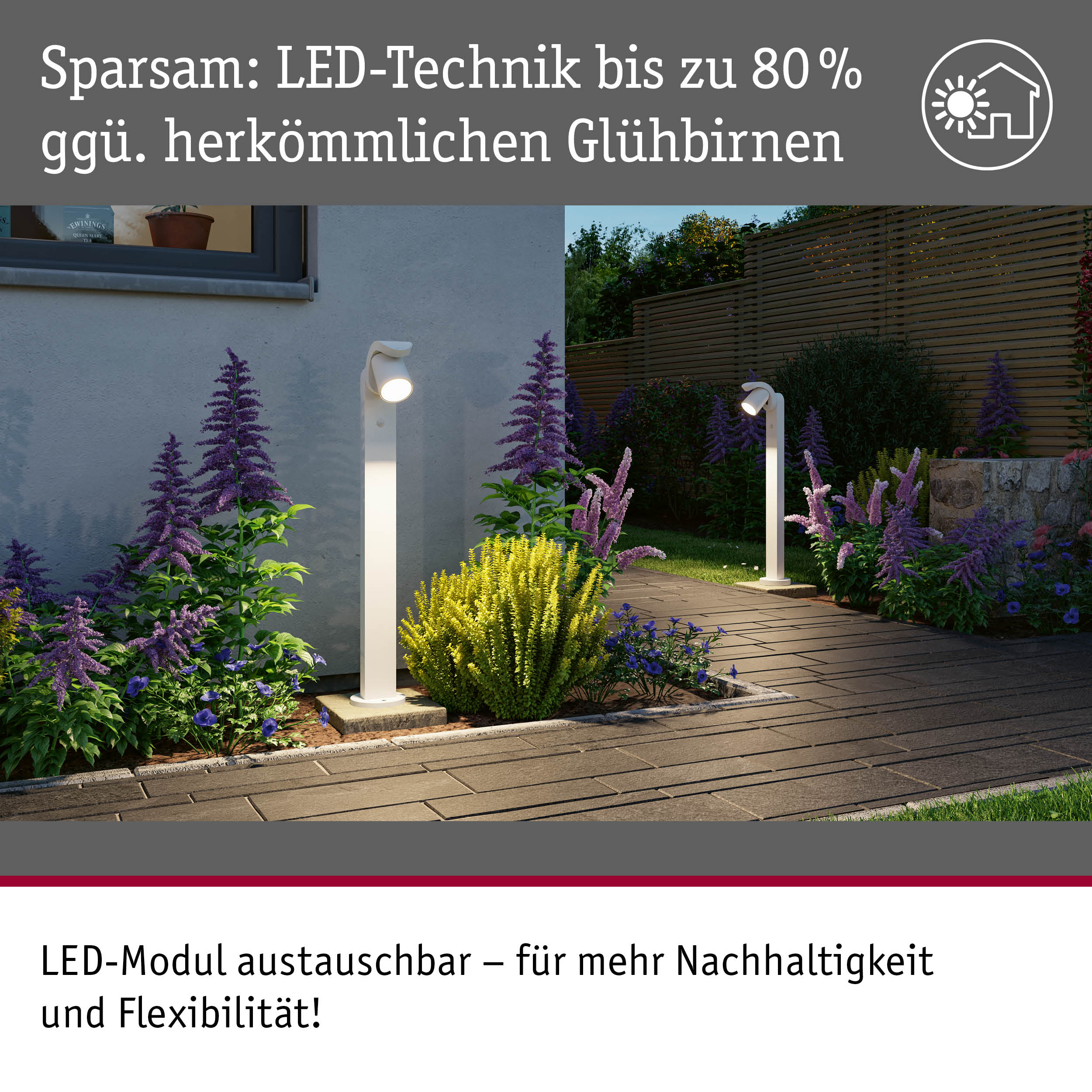 Dwie biale nowoczesne lampy ogrodowe oswietlaja wybrukowana sciezke w otoczeniu kwiatów i sciany domu o zmierzchu.