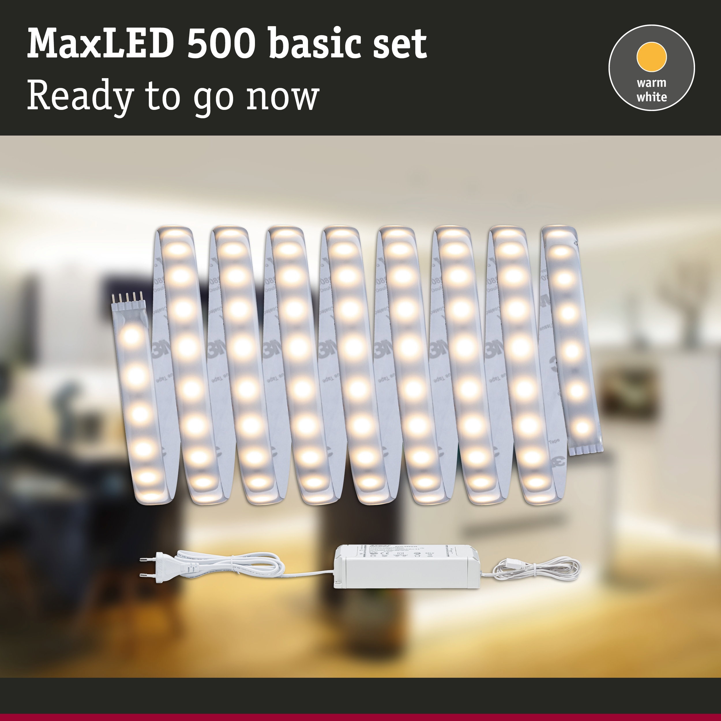 MaxLED 500 Basisset in Warmweiß mit aufgerollten LED-Streifen und Netzteil vor verschwommenem Hintergrund.