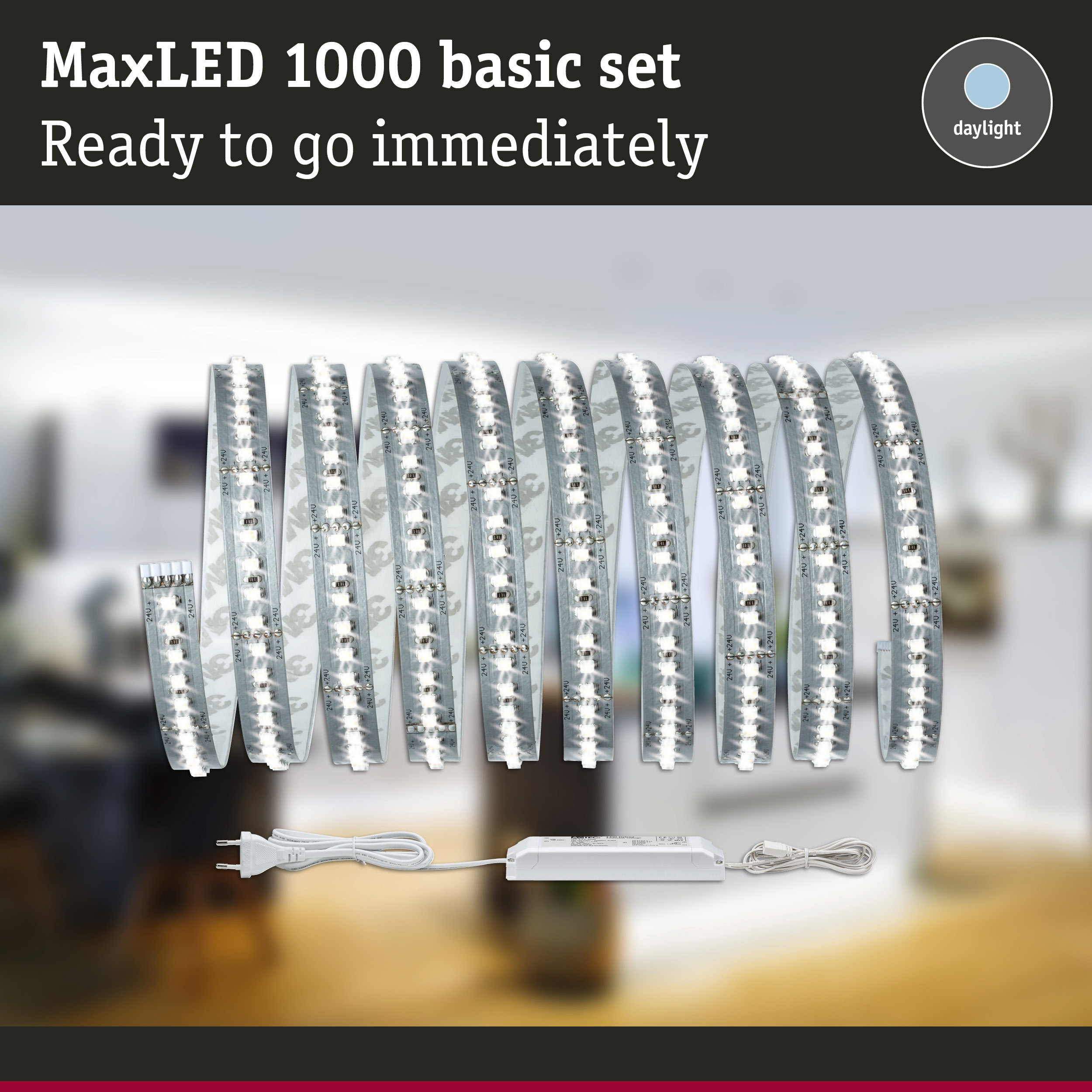 MaxLED 1000 Basis-Set mit aufgerolltem LED-Streifen, Netzteil und Stecker vor verschwommenem Raumhintergrund.