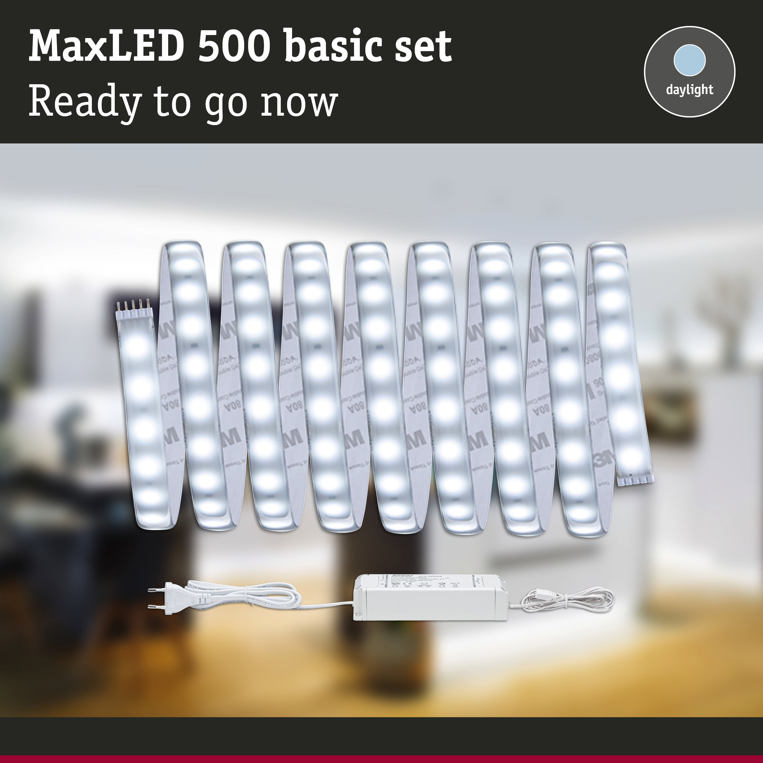 MaxLED 500 Basis-Set in Tageslichtweiß mit LED-Streifen und Netzteil vor verschwommenem Raum.