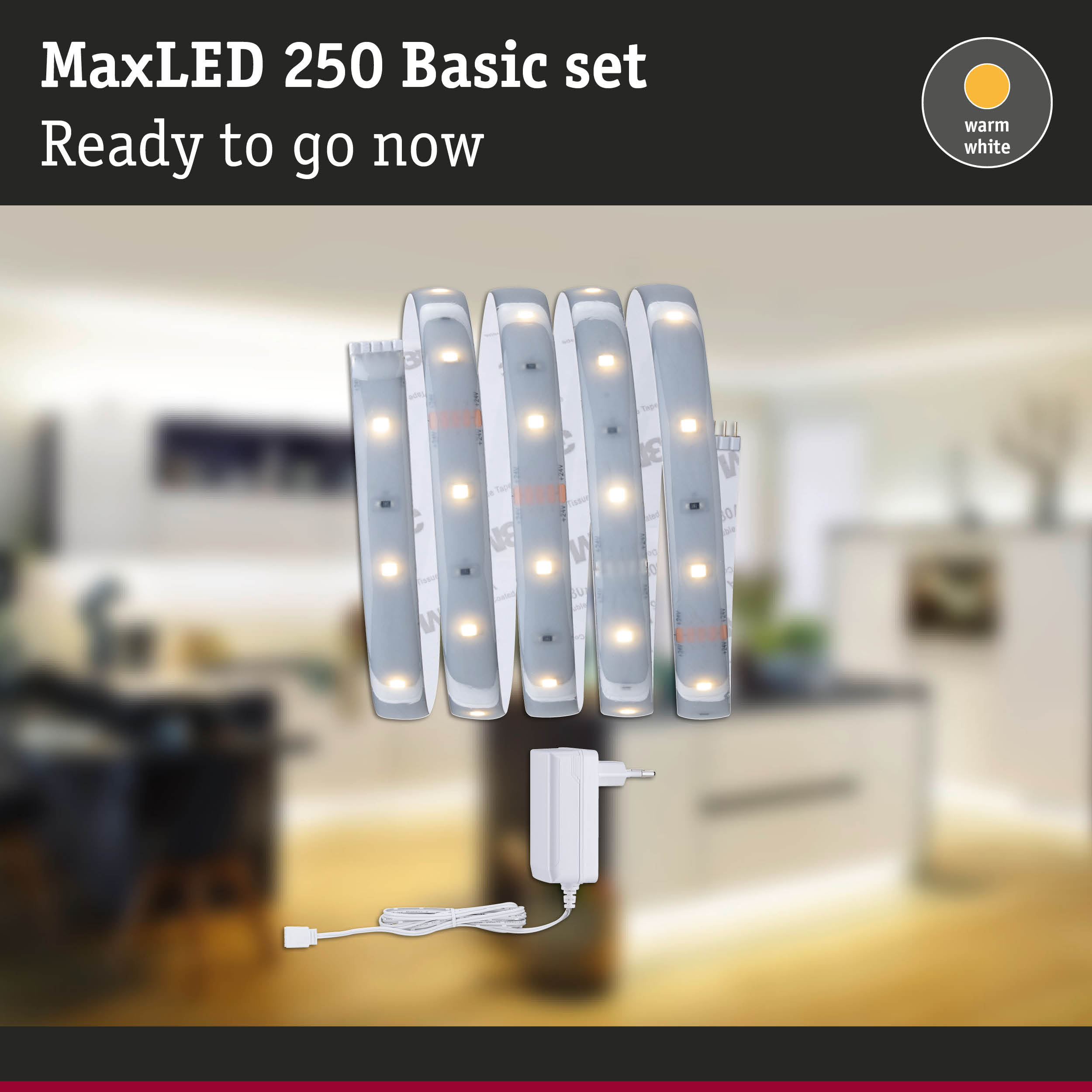 MaxLED 250 Basisset mit warmweißen LED-Streifen und Netzteil vor einer verschwommenen Raumkulisse.