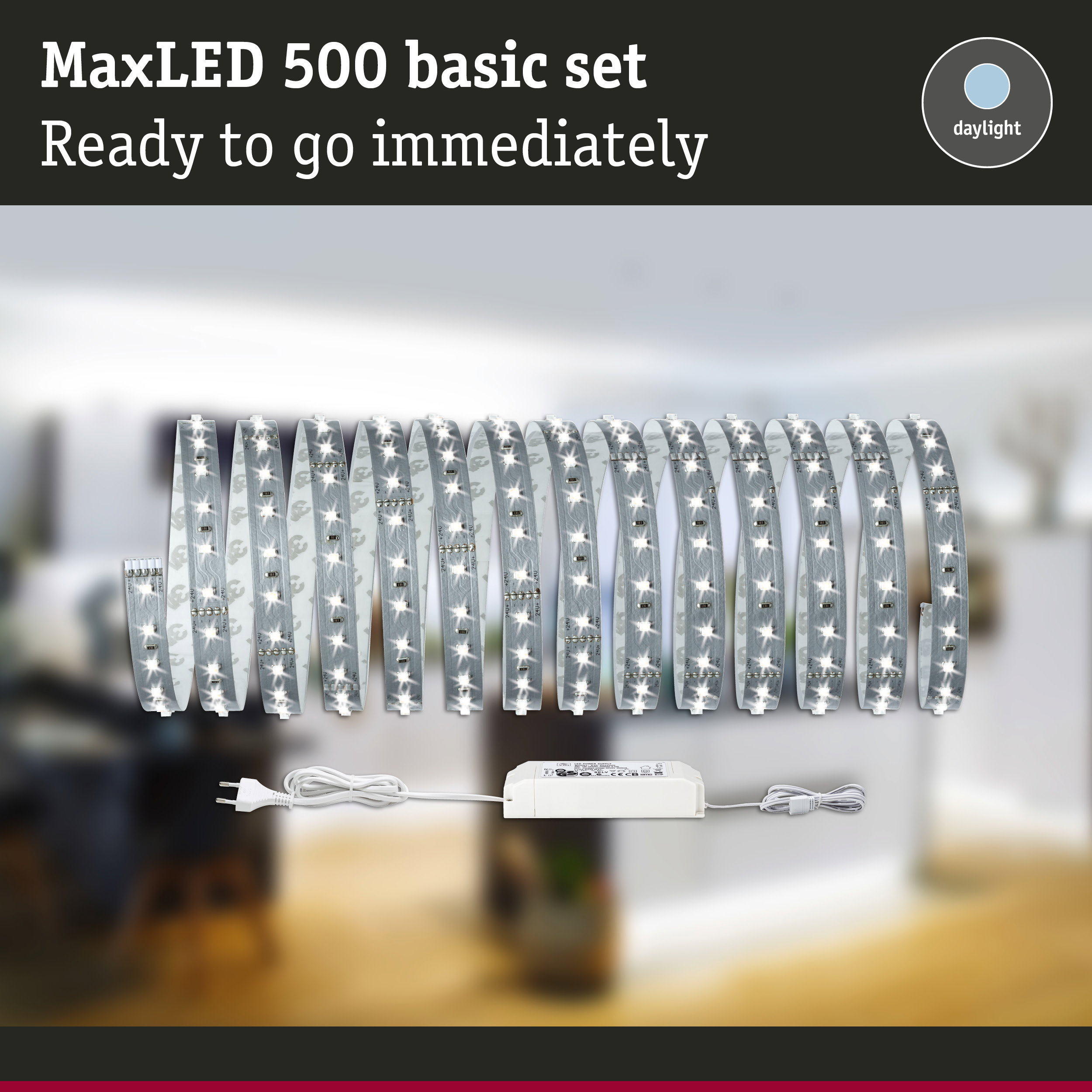 MaxLED 500 Basisset mit einer gerollten, leuchtenden LED-Streife und Netzteil vor verschwommenem Hintergrund.