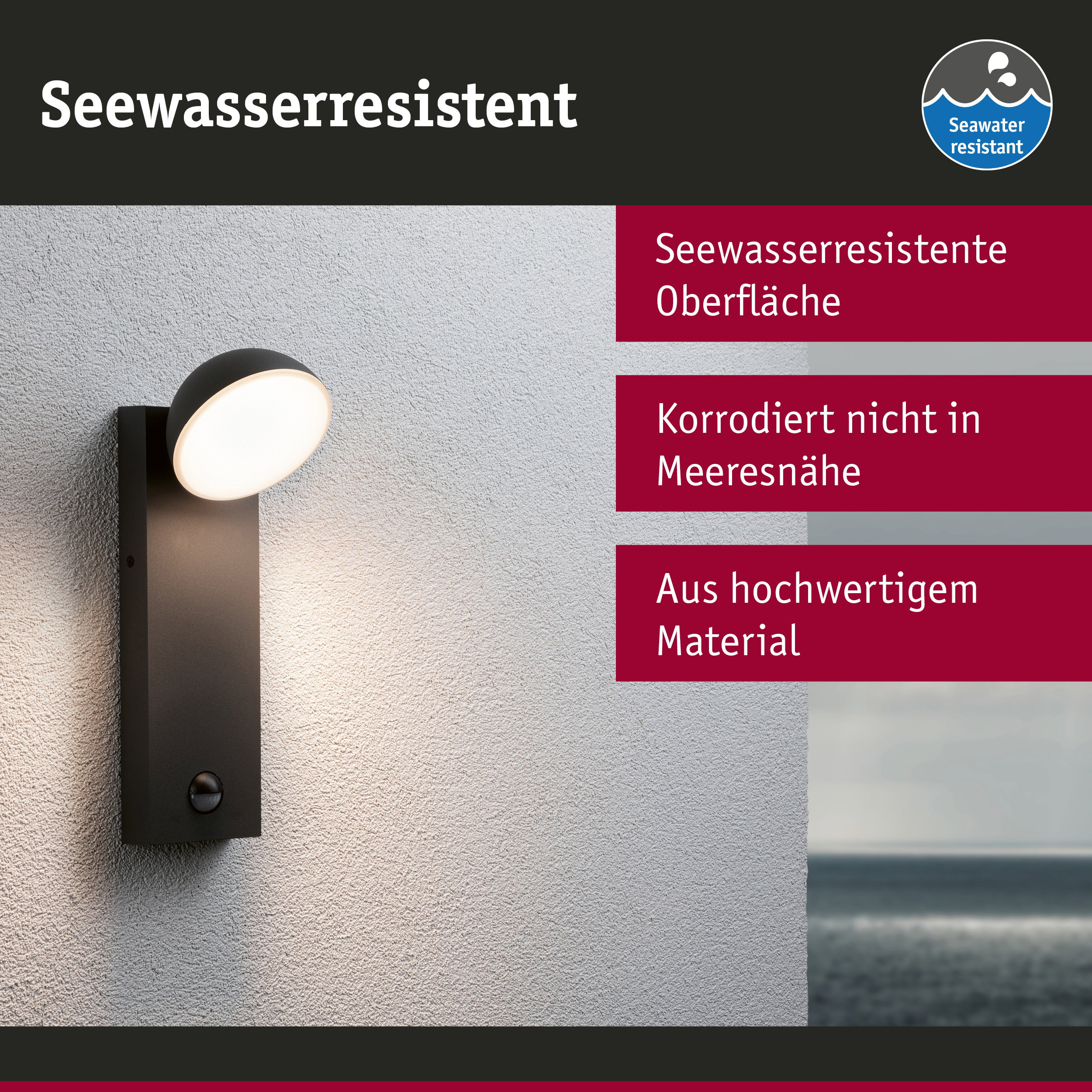 Eine schwarze Wandleuchte an heller Wand mit deutschem Text und Meeresblick im Hintergrund.