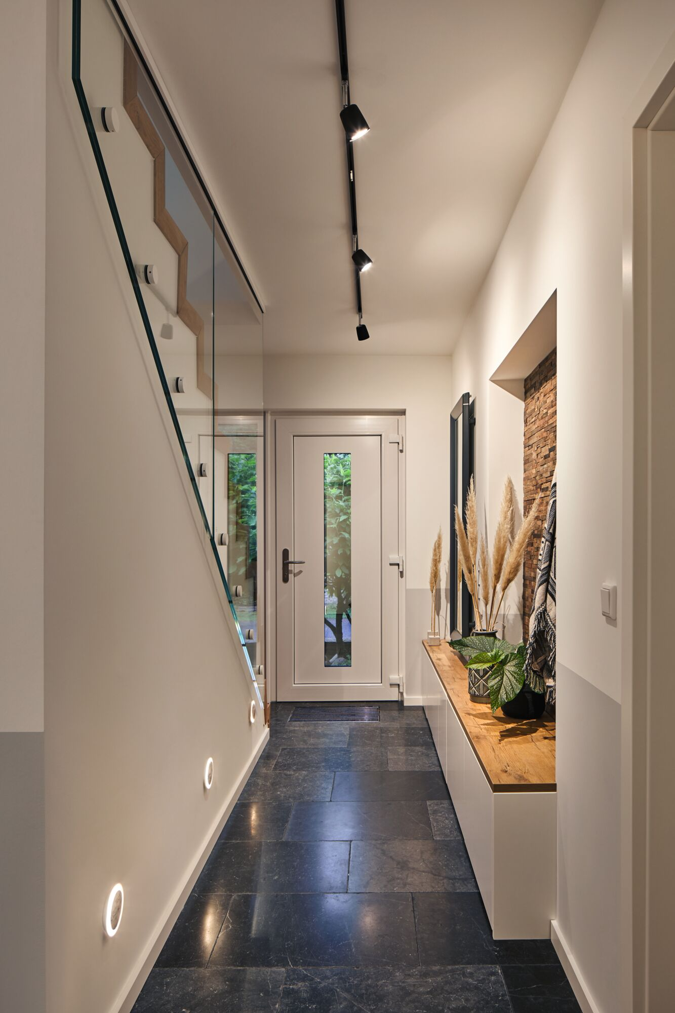 Moderne Diele mit GlasgelÃ¤nder an der Treppe, dunklem Steinboden und Holzsitzbank mit Pflanzen.