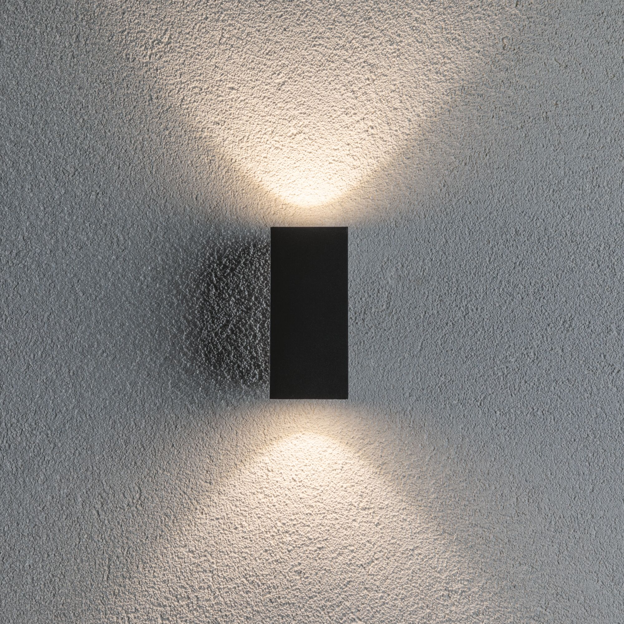 Czarna lampa ścienna rzuca światło w górę i w dół na szarą, teksturowaną ścianę.