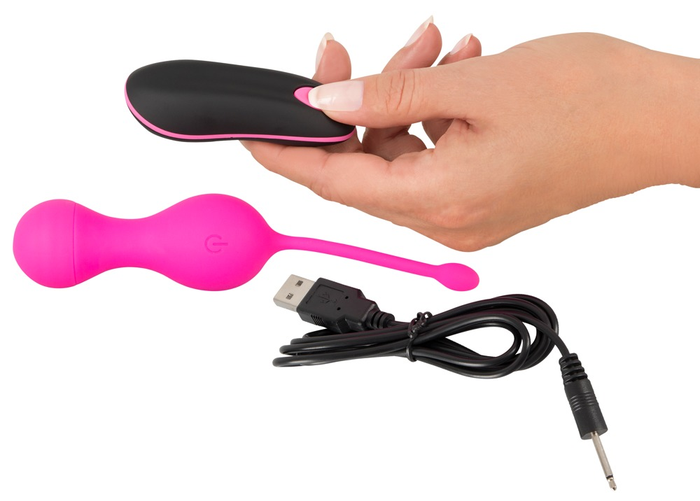 Hand hält eine schwarze Fernbedienung neben einem pinken vibrierenden Ei und einem USB-Kabel.