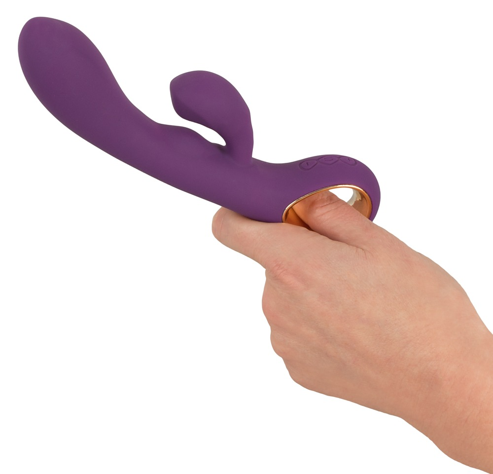 Eine Hand hält einen violetten Vibrator mit einem goldenen Ring vor weißem Hintergrund.