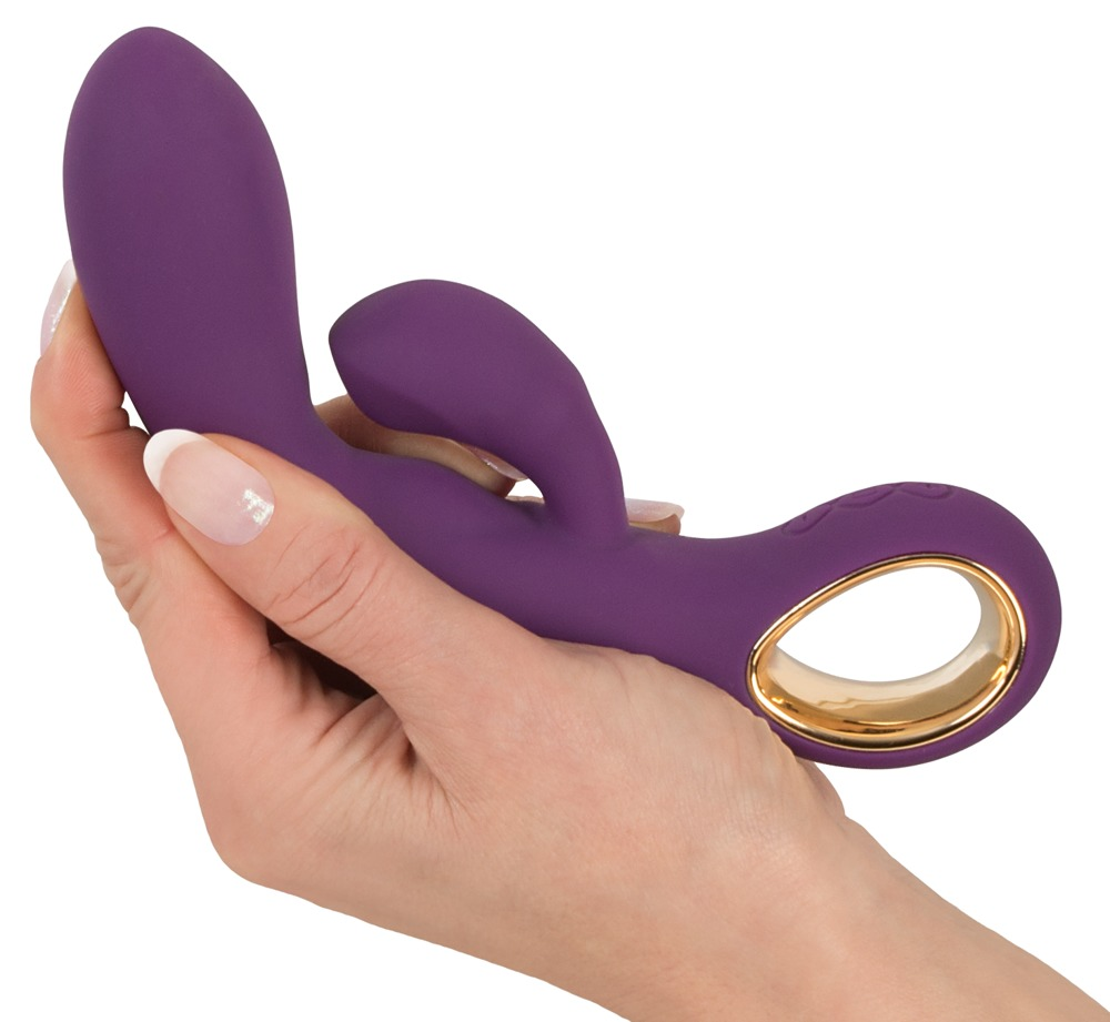 Eine Hand hält ein ergonomisches, violettes Silikon-Doppelstimulationsspielzeug mit Goldring.