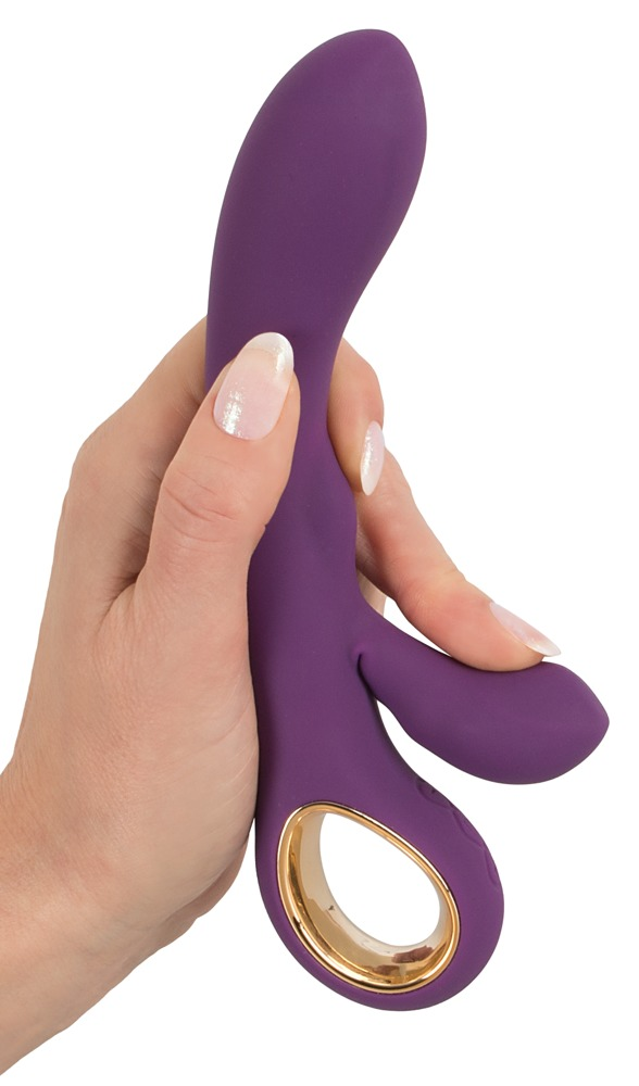 Eine Hand hält ein violettes, geschwungenes Silikon-Sexspielzeug mit goldenem Ring auf weißem Hintergrund.