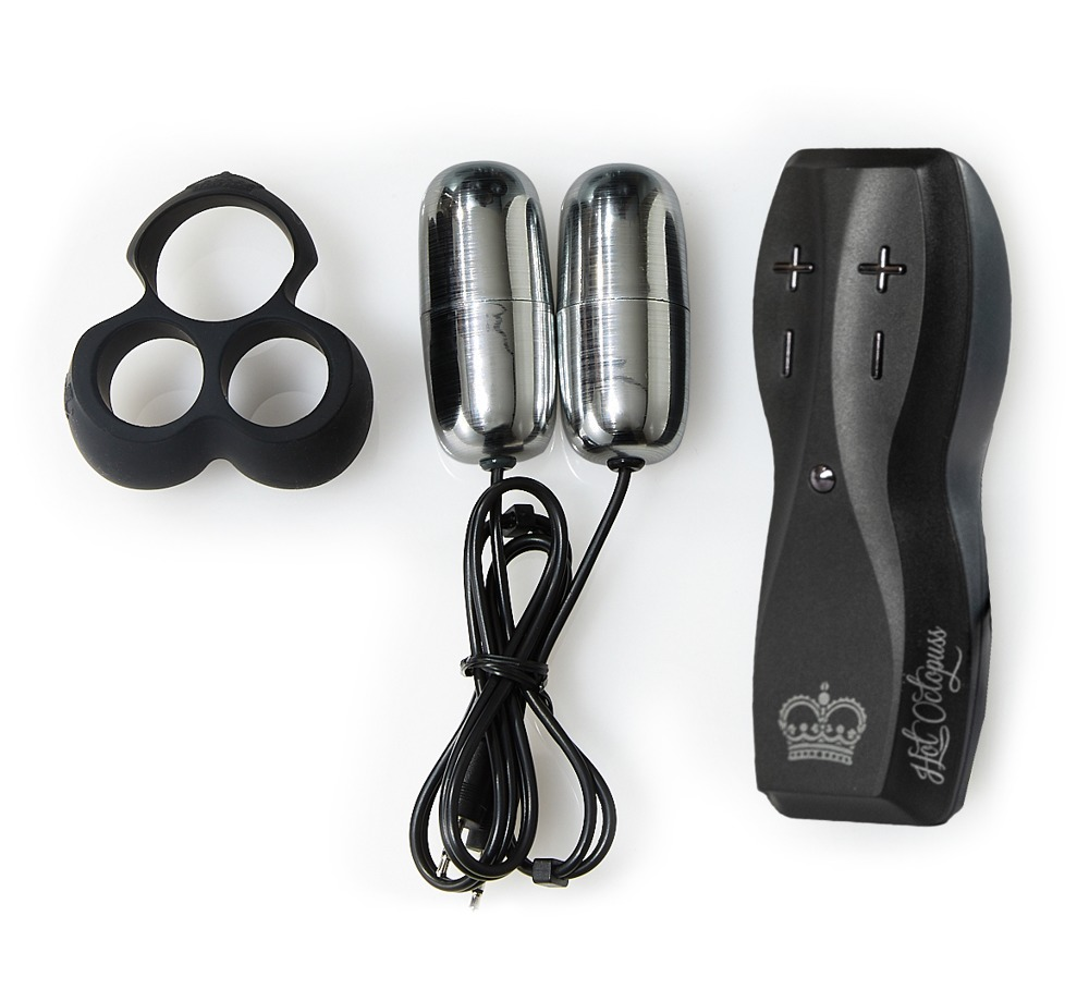 Un anillo triple negro, dos balas vibradoras plateadas con cables y un control remoto negro sobre blanco.