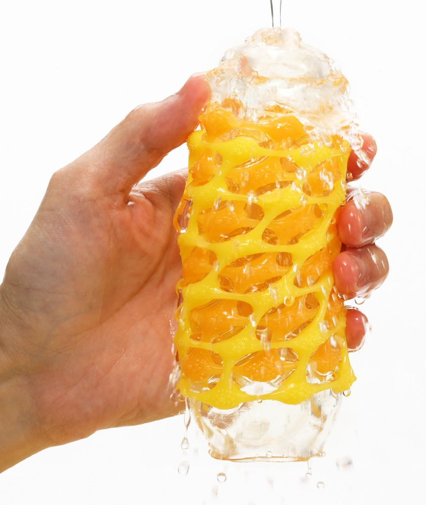 Eine Hand wäscht einen transparenten Behälter mit einem gelben Netzmuster unter fließendem Wasser.