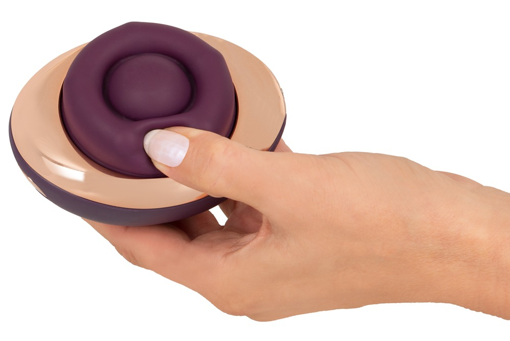 Eine Hand hält ein rundes, violettes und roségoldenes Wellness-Gerät.