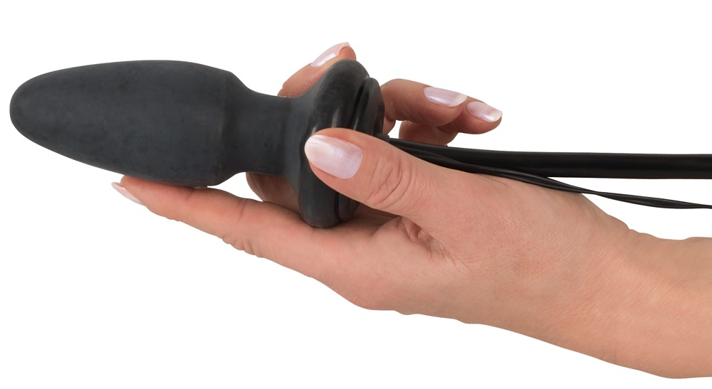 Eine Hand hält einen schwarzen, konischen Analplug mit Kabel.