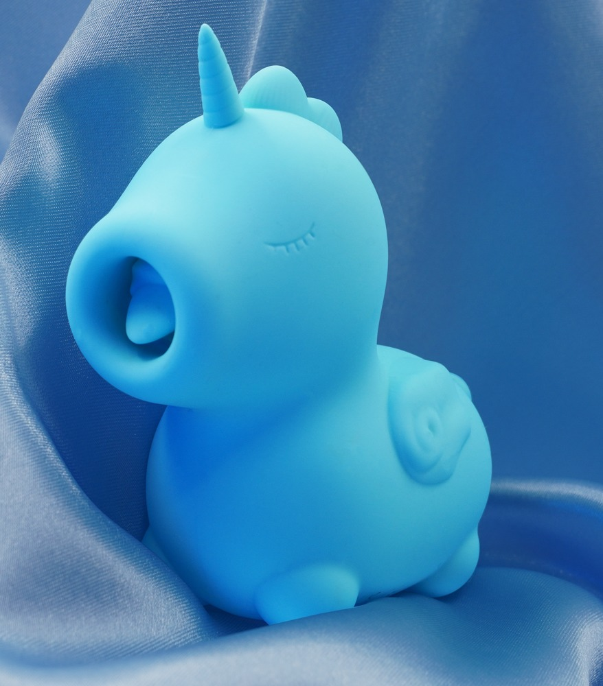 Ein hellblaues Einhorn-Spielzeug aus Silikon steht vor glänzenden blauen Stoff.