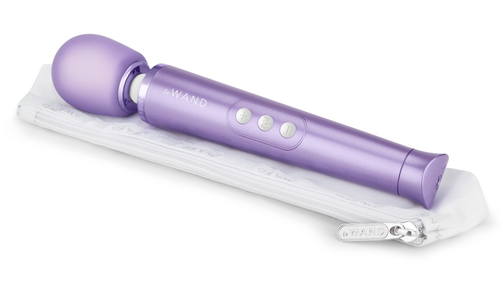 Ein lilafarbener Zauberstab-Vibrator liegt auf einer weißen Stofftasche mit Reißverschluss vor weißem Hintergrund.