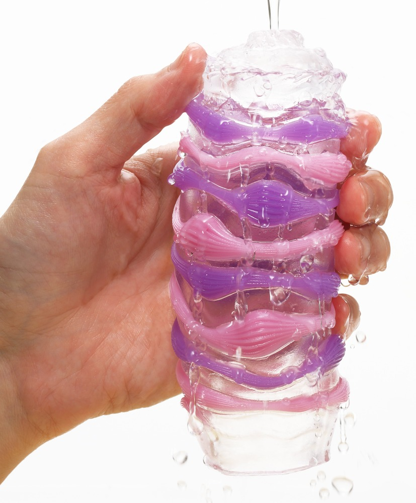 Eine Hand hält einen nassen, durchsichtigen Zylinder mit lila und rosa Streifen, während Wasser darüber gießt.