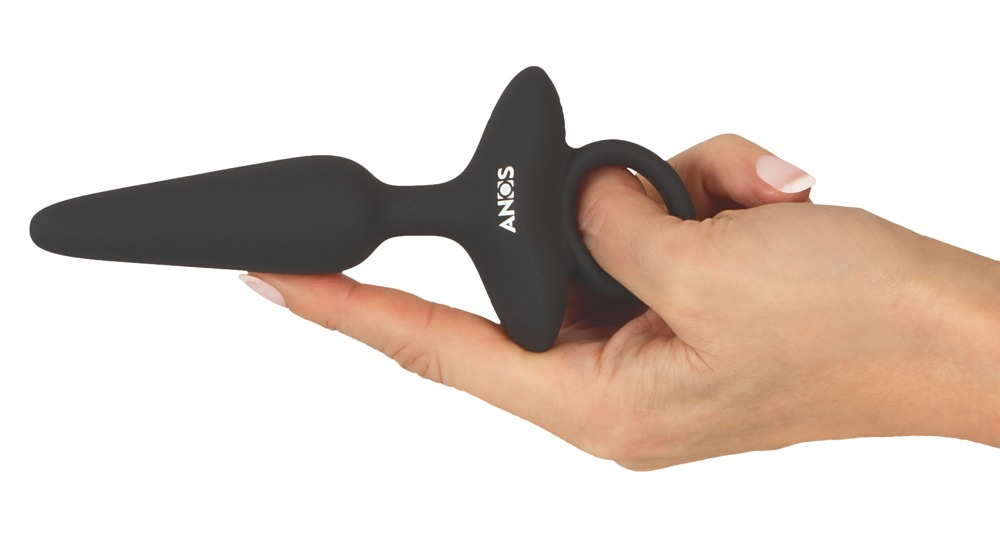Eine Hand hält einen schwarzen Silikon-Anaplug mit T-förmiger Basis und Fingerring vor weißem Hintergrund.