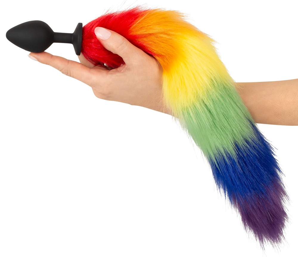 Eine Hand hält einen schwarzen Analplug mit einem langen, regenbogenfarbenen Kunstfellsatz.