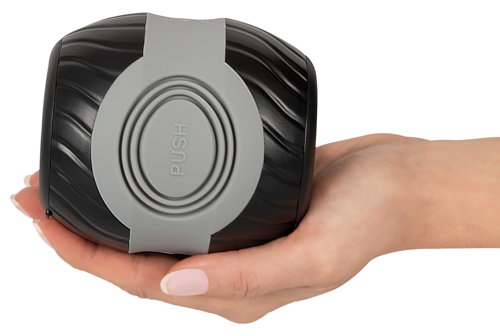Eine Hand hält ein rundes schwarzes Gadget mit einem grauen, runden PUSH-Knopf.