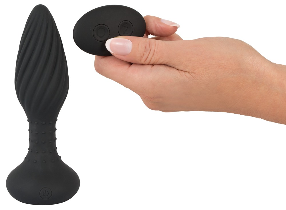 Ein schwarzer spiralförmiger Analklotz steht neben einer Hand, die eine ovale Fernbedienung hält.