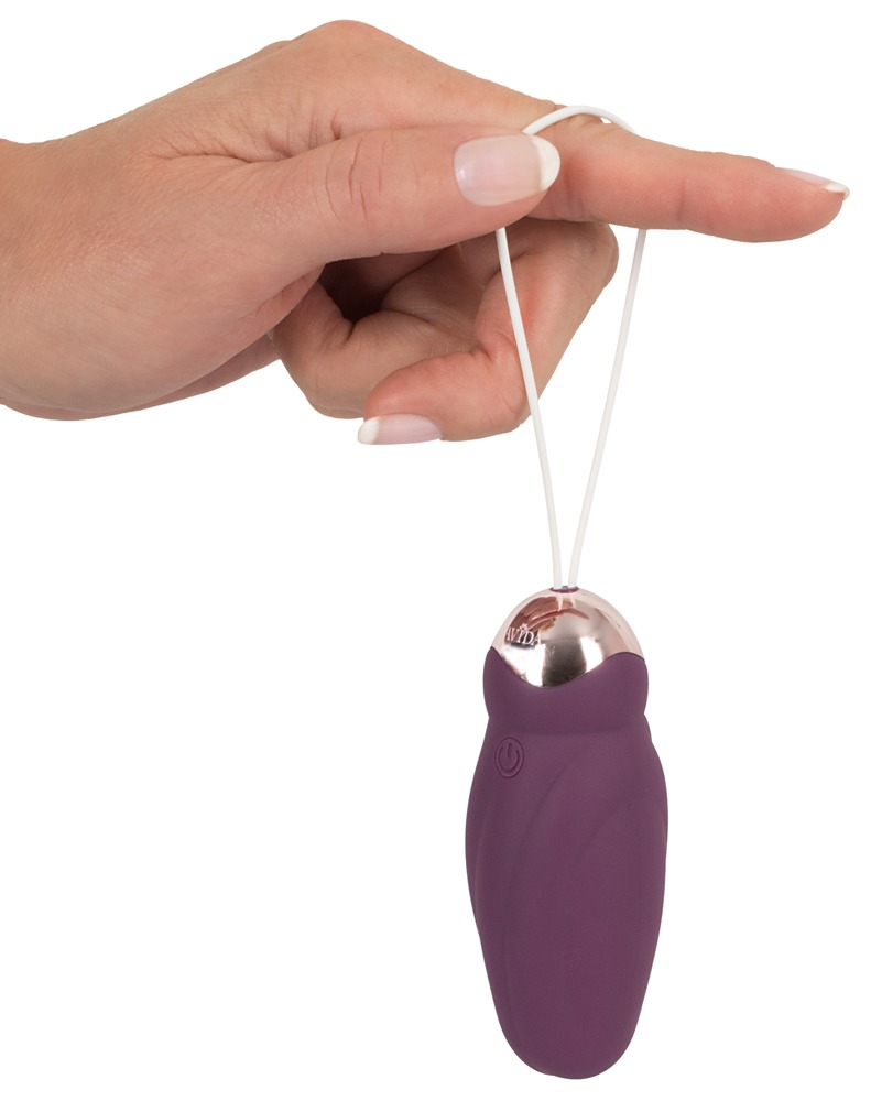 Eine Hand hält ein violettes, eiförmiges Gerät mit einer weißen Kordel vor weißem Hintergrund.