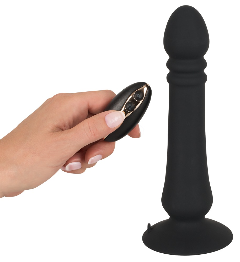 Eine Hand hält eine kleine ovale Fernbedienung vor einem schwarzen Dildo auf weißem Hintergrund.