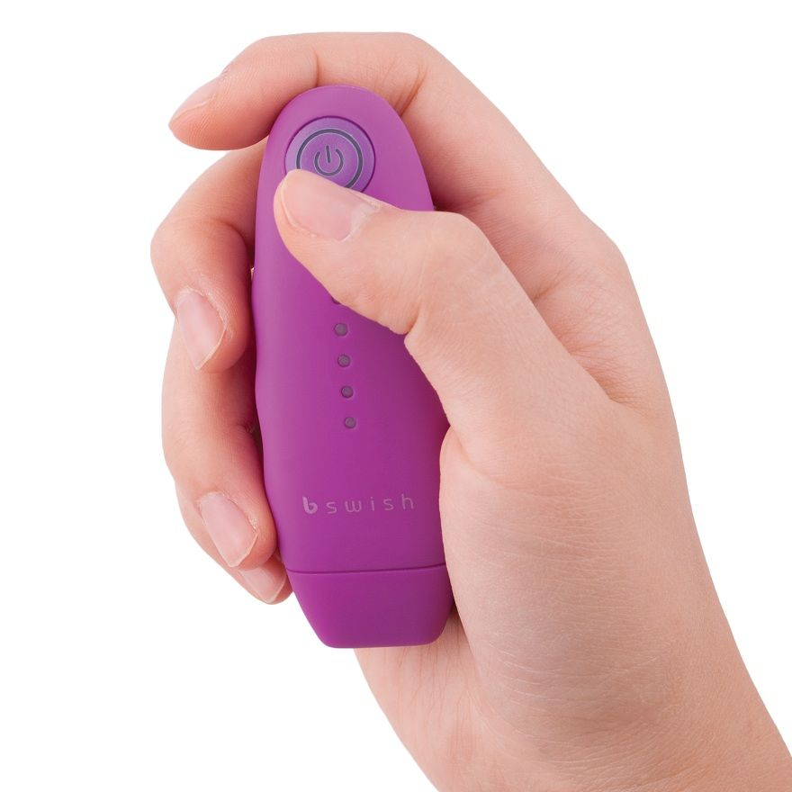 Una mano sostiene un pequeño dispositivo violeta en forma de huevo con un botón de encendido y el logotipo de bswish.
