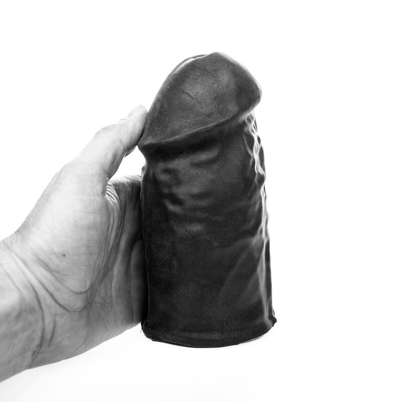 Eine Hand hält ein dunkles, strukturiertes Objekt in Form eines Phallus vor weißem Hintergrund.