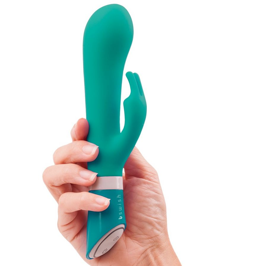 Una mano sostiene un dispositivo de bienestar verde azulado con botones sobre fondo blanco.