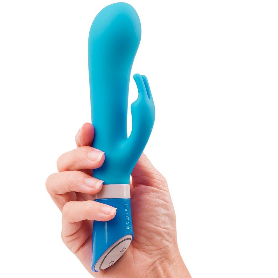 Una mano sosteniendo un vibrador azul y ergonómico con un pequeño accesorio sobre fondo blanco.
