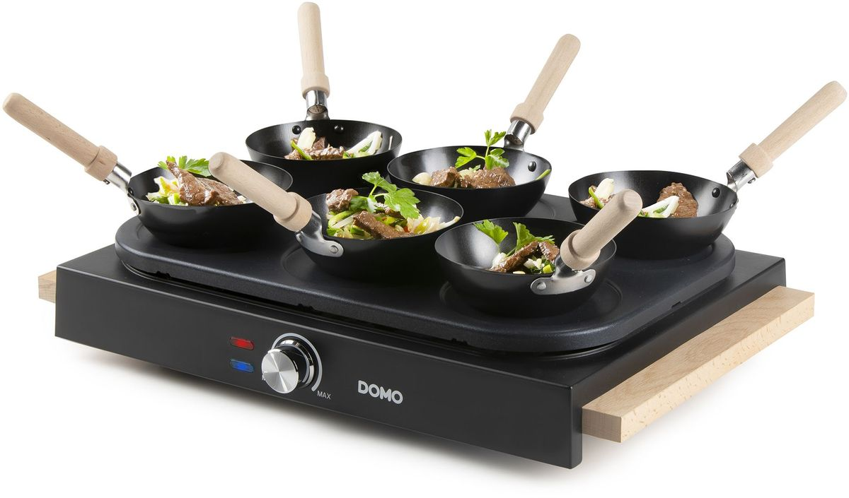 Ein elektrischer Wok-Grill mit sechs kleinen schwarzen Pfannen, Holzgriffen und rohem Gemüse mit Fleisch.